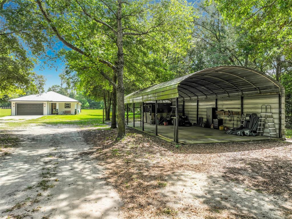 A metal carport stands next to a dirt driveway leading to a detached garage building — 34814 WILLIAM LANE, EUSTIS, FL