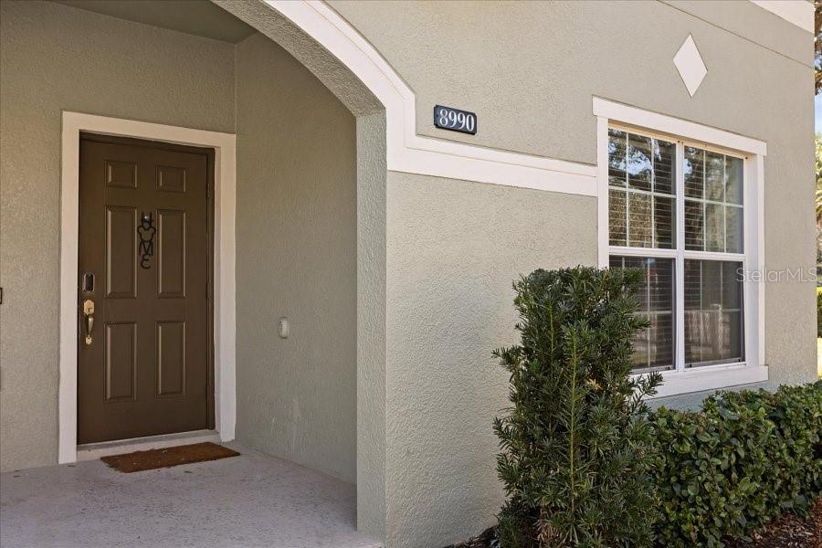 A front entryway features a brown door, a window, and a house number on stucco — 8990 CUBAN PALM ROAD, KISSIMMEE, FL