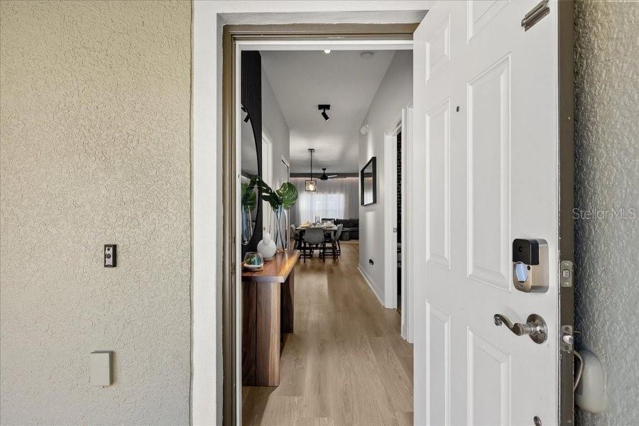 An open front door reveals a hallway with light wood flooring leading to a dining area — 8990 CUBAN PALM ROAD, KISSIMMEE, FL