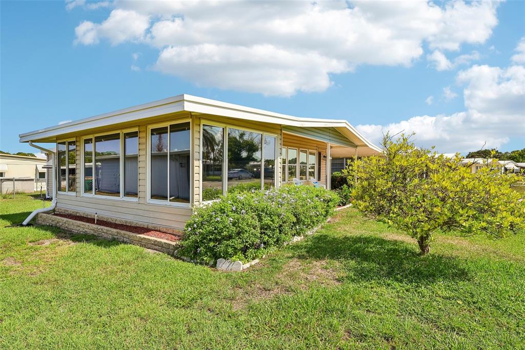 A single-story manufactured home with light siding, large windows, and a surrounding grassy yard — 1433 APACHE CIRCLE, TAVARES, FL