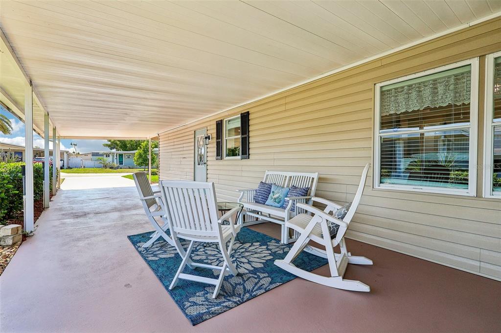 A covered patio features a blue floral rug, white chairs, and a bench against siding — 1433 APACHE CIRCLE, TAVARES, FL