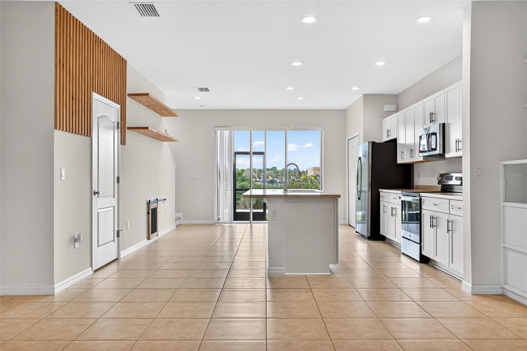 A kitchen with white cabinets, a center island, and tile flooring opens to a patio — 8667 CANYON CREEK TRAIL, PARRISH, FL