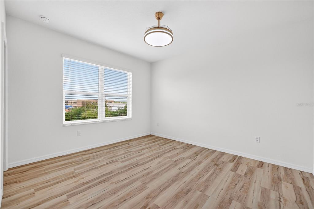 An empty bedroom features white walls, light wood-look flooring, and a modern ceiling fan light — 8667 CANYON CREEK TRAIL, PARRISH, FL