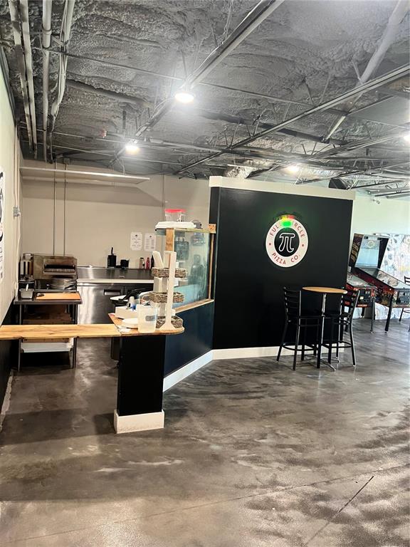 A commercial kitchen area features a pizza counter, black wall with logo, and concrete flooring — 235 NE WATULA AVENUE, OCALA, FL