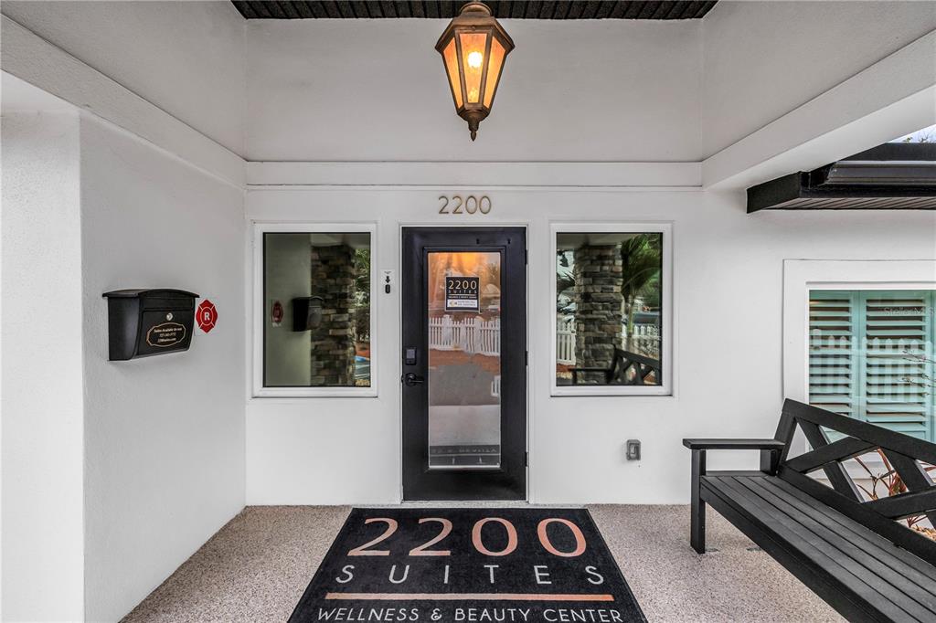 The entrance to a building features a black door, a welcome mat, and a bench — 2200 49TH STREET N, ST PETERSBURG, FL