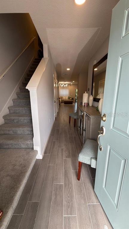 A hallway with gray wood-look tile flooring leads to a front door and a chair — 5007 PRAIRIE PRESERVE RUN, ST CLOUD, FL