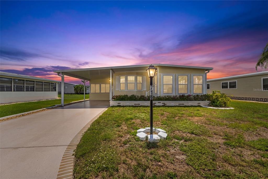 A single-story manufactured home with a carport and a front yard at sunset — 716 SANCHEZ CIRCLE, NORTH PORT, FL