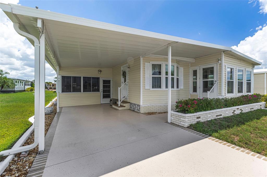 A light-colored mobile home features a large covered carport and a brick-bordered flower bed — 716 SANCHEZ CIRCLE, NORTH PORT, FL