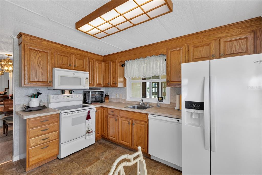 A kitchen features oak cabinets, white appliances, a tiled floor, and a rectangular ceiling light — 716 SANCHEZ CIRCLE, NORTH PORT, FL