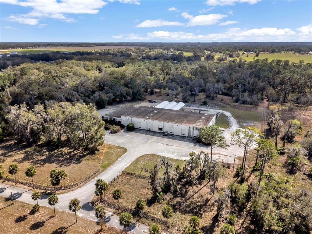 An aerial view shows a large industrial warehouse building surrounded by trees and paved parking — 34135 CARDINAL LANE, EUSTIS, FL