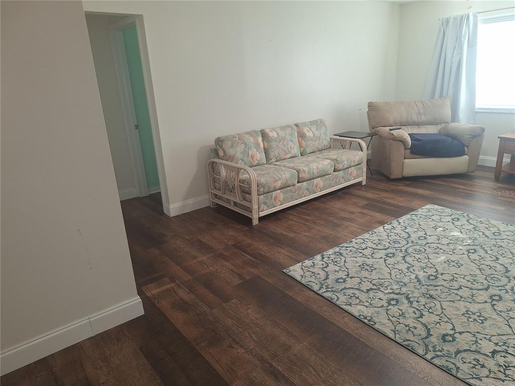 A living room features wood-look flooring, a floral sofa, a beige recliner, and an area rug — 8447 AUSTIN N UNIT 8447, PINELLAS PARK, FL