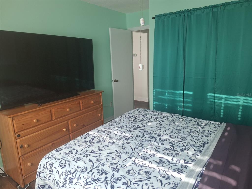 A bedroom features a wooden dresser, a large television, and a bed with patterned bedding — 8447 AUSTIN N UNIT 8447, PINELLAS PARK, FL