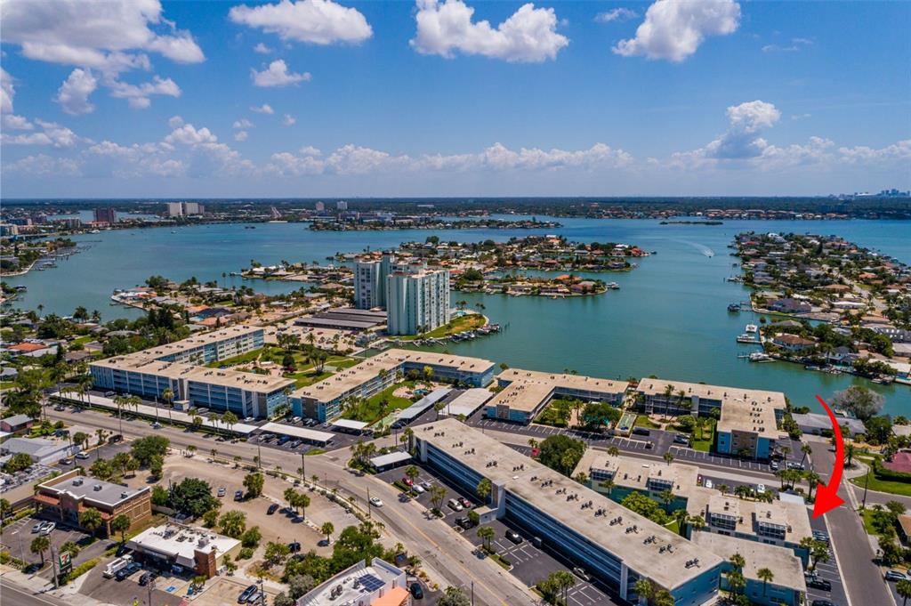 An aerial view shows a multi-story apartment complex near a bay with a red arrow — 6000 2ND STREET E UNIT 6, ST PETE BEACH, FL