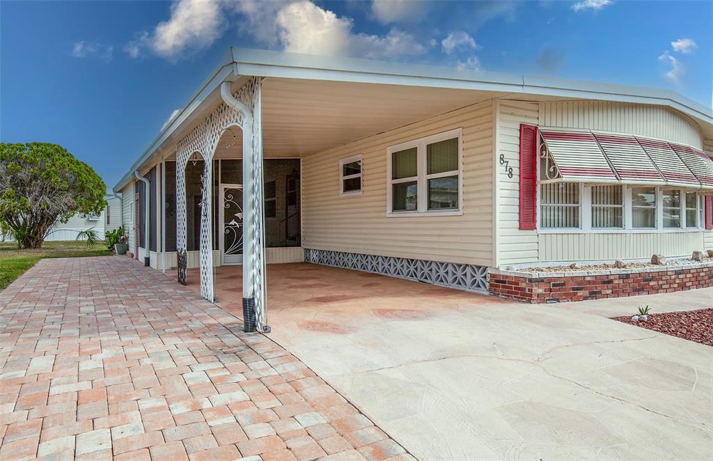 A mobile home exterior features a paved driveway, a covered carport, and red window shutters — 878 JOLANDA CIRCLE, VENICE, FL