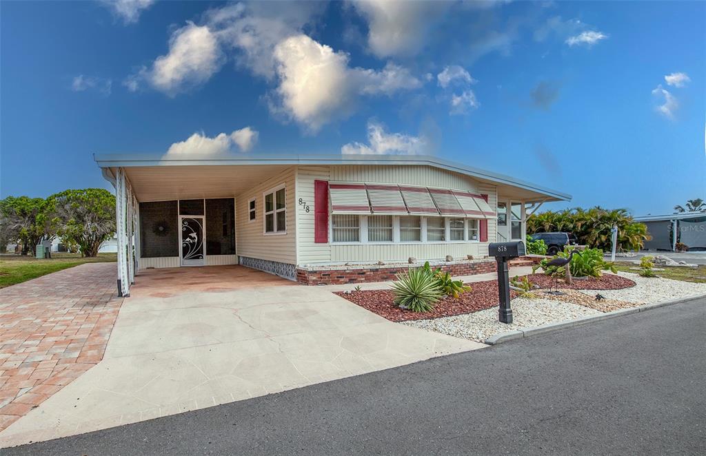 A single-story manufactured home features a carport, brick skirting, and a front yard with landscaping — 878 JOLANDA CIRCLE, VENICE, FL