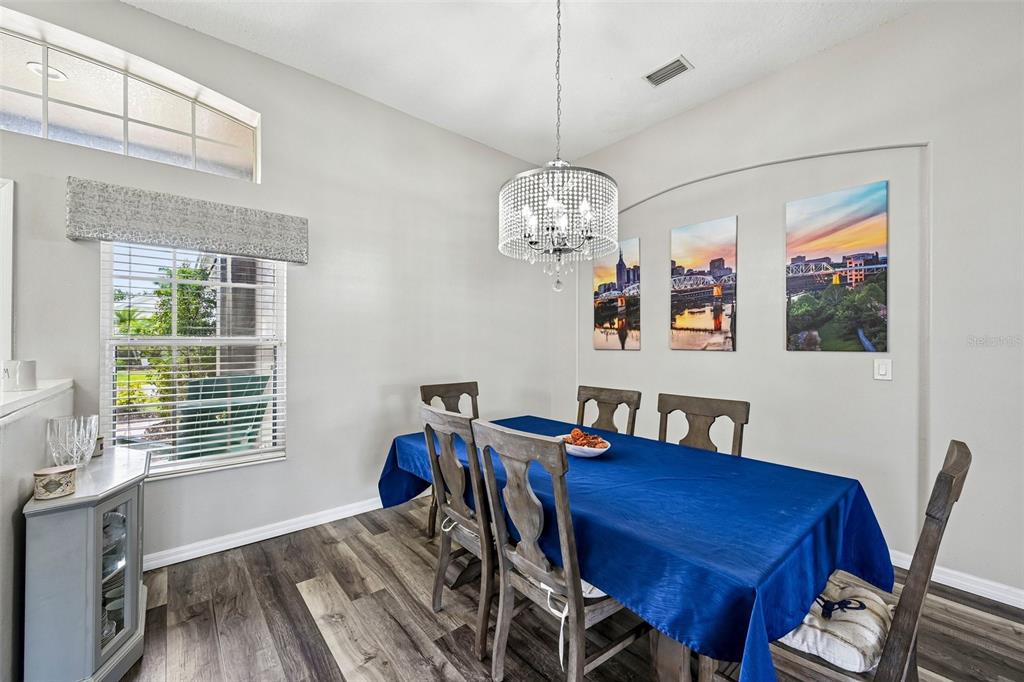 A dining room features a blue tablecloth, a crystal chandelier, and three wall-mounted cityscapes — 2910 127TH PLACE E, PARRISH, FL