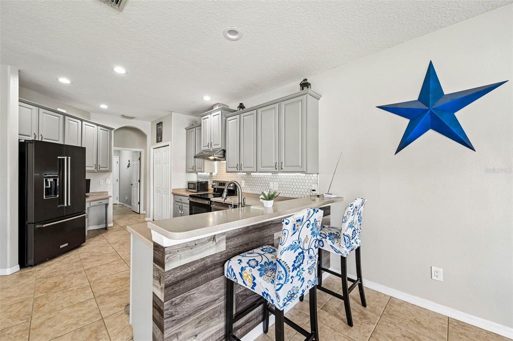A kitchen features gray cabinets, a breakfast bar with patterned stools, and a blue star decoration — 2910 127TH PLACE E, PARRISH, FL