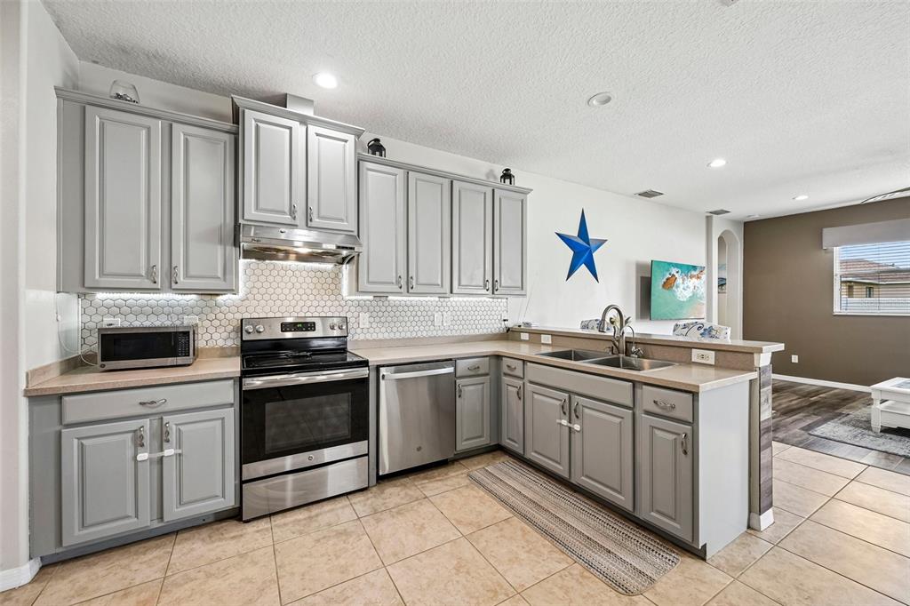 A kitchen features gray cabinets, stainless steel appliances, a tiled backsplash, and light-colored countertops — 2910 127TH PLACE E, PARRISH, FL