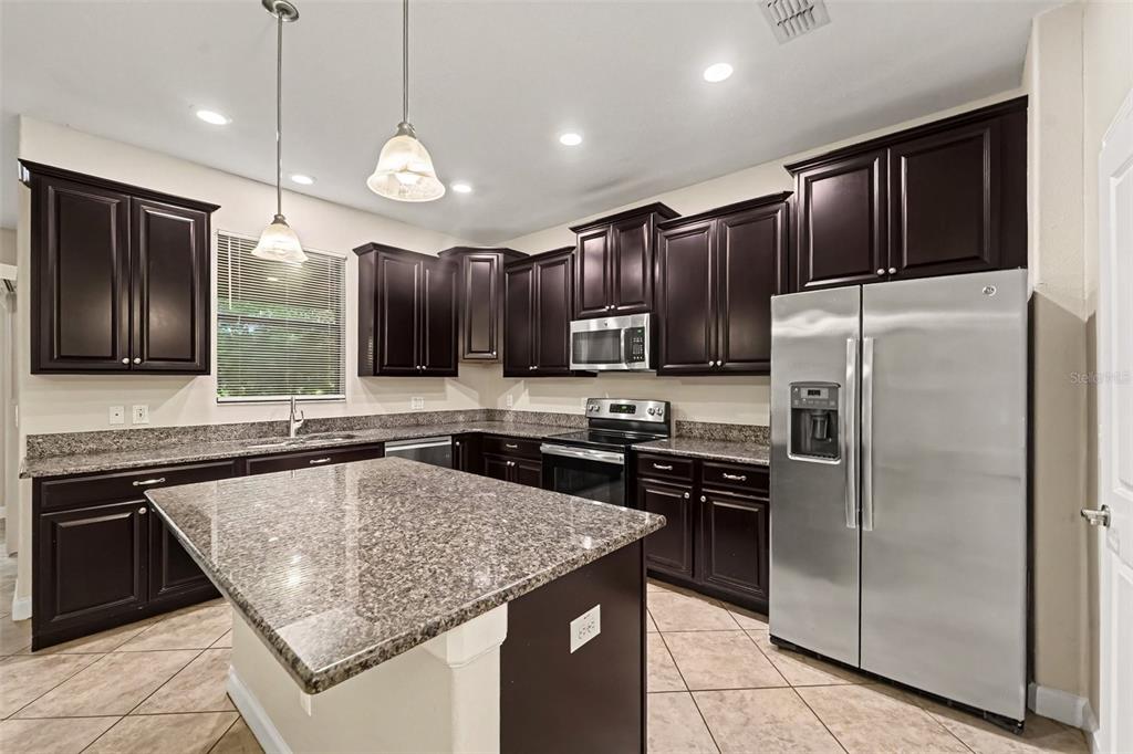 A kitchen features dark wood cabinets, granite countertops, a center island, and stainless steel appliances — 17335 OLD TOBACCO ROAD, LUTZ, FL