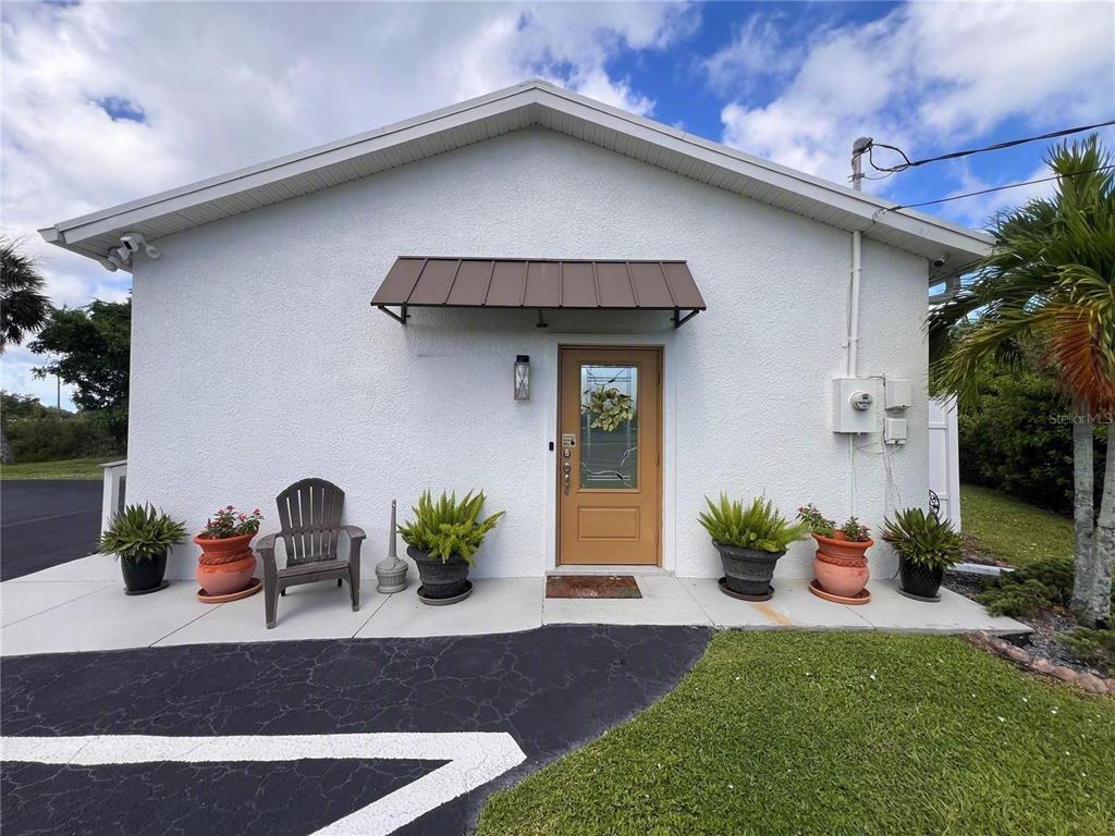 A white stucco building exterior features a brown door, metal awning, and potted plants — 180 RIO VILLA DRIVE, PUNTA GORDA, FL