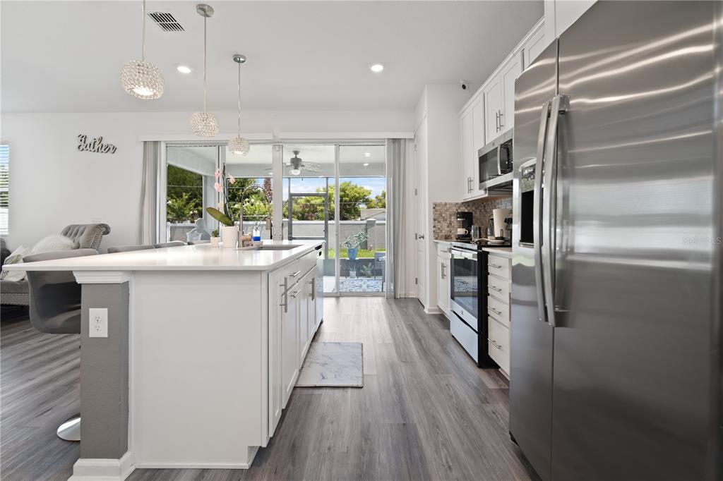 A modern kitchen features white cabinetry, a large island, stainless steel appliances, and wood-look flooring — 1125 MATTIE POINTE BOULEVARD, AUBURNDALE, FL