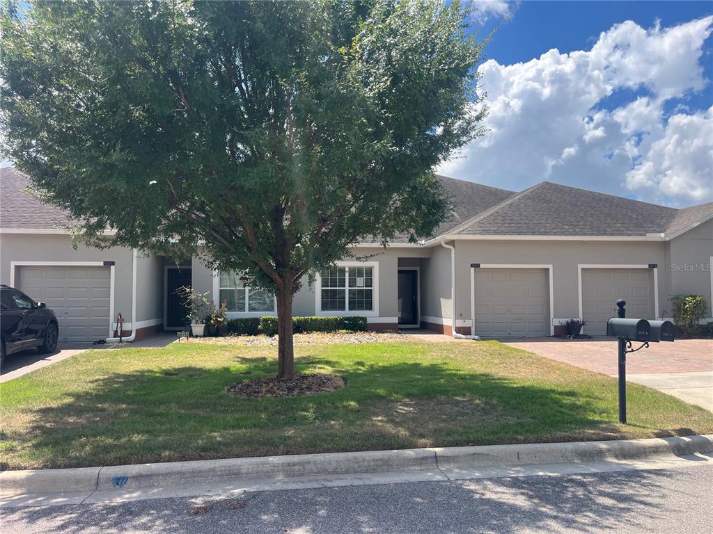 A single-story duplex with gray stucco walls, three garage doors, and a large front tree — 3615 SOLANA CIRCLE UNIT B, CLERMONT, FL