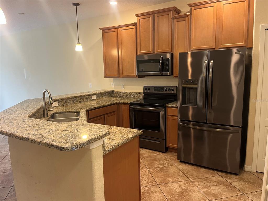 A kitchen features wood cabinets, granite countertops, stainless steel appliances, and tile flooring — 3615 SOLANA CIRCLE UNIT B, CLERMONT, FL