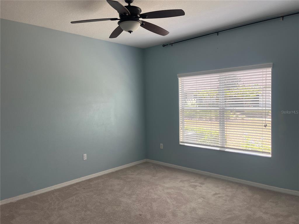 An empty bedroom features light blue walls, beige carpeting, a ceiling fan, and a window — 3615 SOLANA CIRCLE UNIT B, CLERMONT, FL