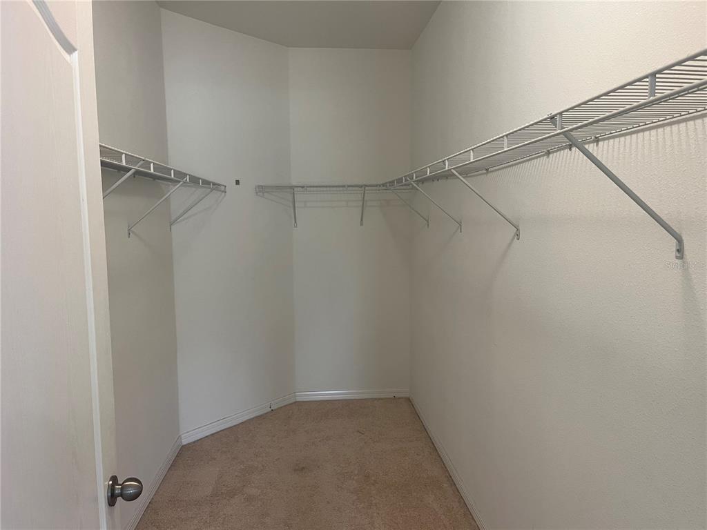 A walk-in closet features white wire shelving installed along the walls over beige carpet — 3615 SOLANA CIRCLE UNIT B, CLERMONT, FL