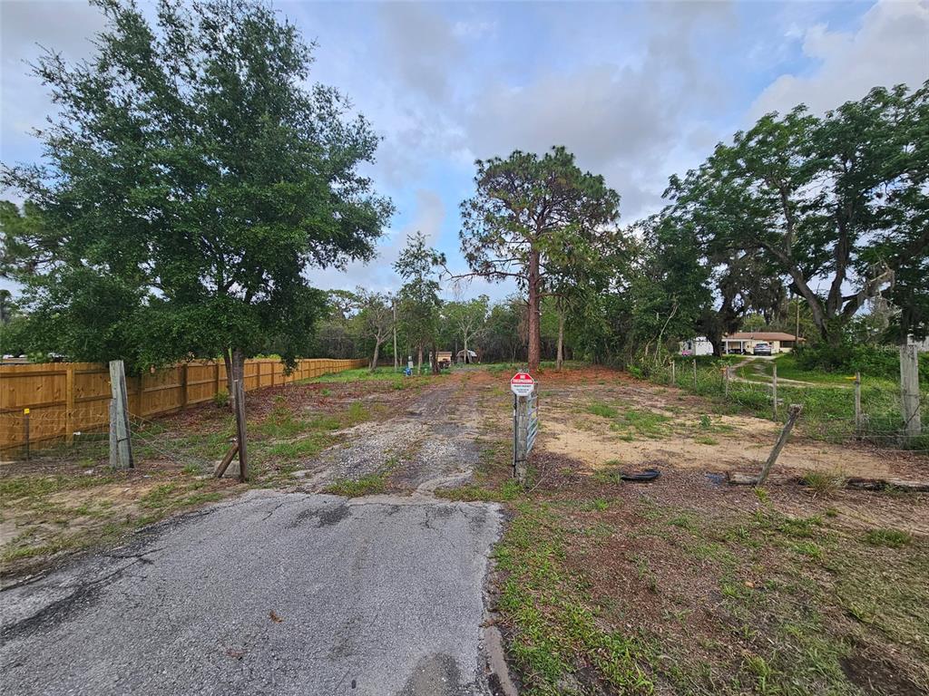A gravel driveway leads into a vacant, grassy lot bordered by trees and a wooden fence — 17132 RIDGELINE TRAIL, HUDSON, FL