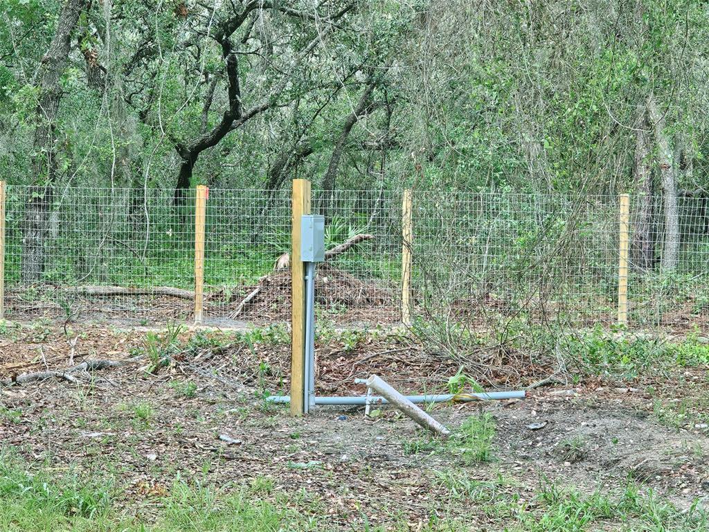 A gray electrical box is mounted on a wooden post in front of a wire fence — 17132 RIDGELINE TRAIL, HUDSON, FL