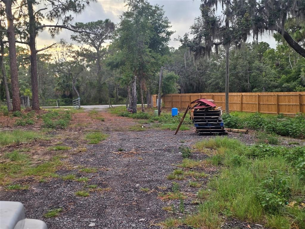 A gravel driveway leads toward a wooden fence and a stack of pallets outdoors — 17132 RIDGELINE TRAIL, HUDSON, FL