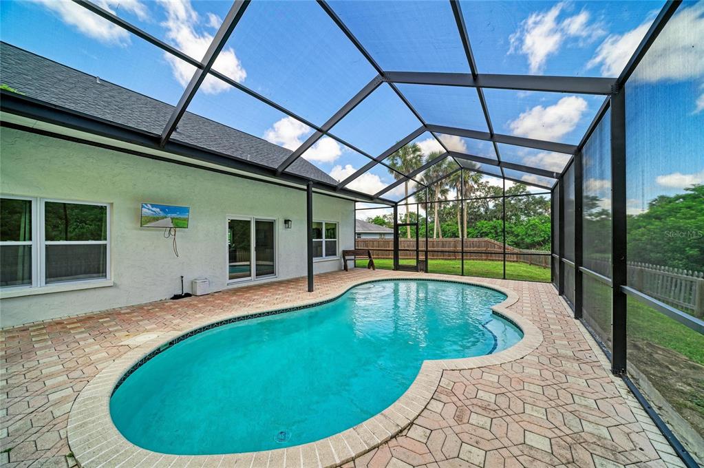 A screened-in patio features a kidney-shaped swimming pool and brick pavers against a house exterior — 3220 37TH TERRACE E, BRADENTON, FL