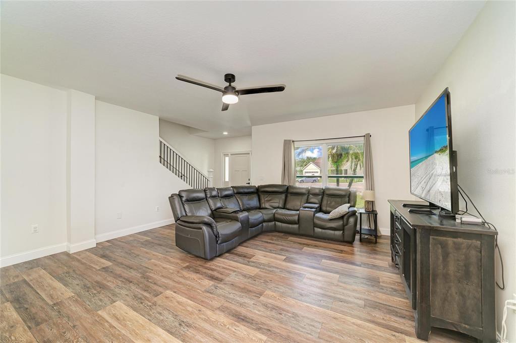 A living room features wood-look flooring, a large gray sectional sofa, and a wall-mounted television — 3220 37TH TERRACE E, BRADENTON, FL