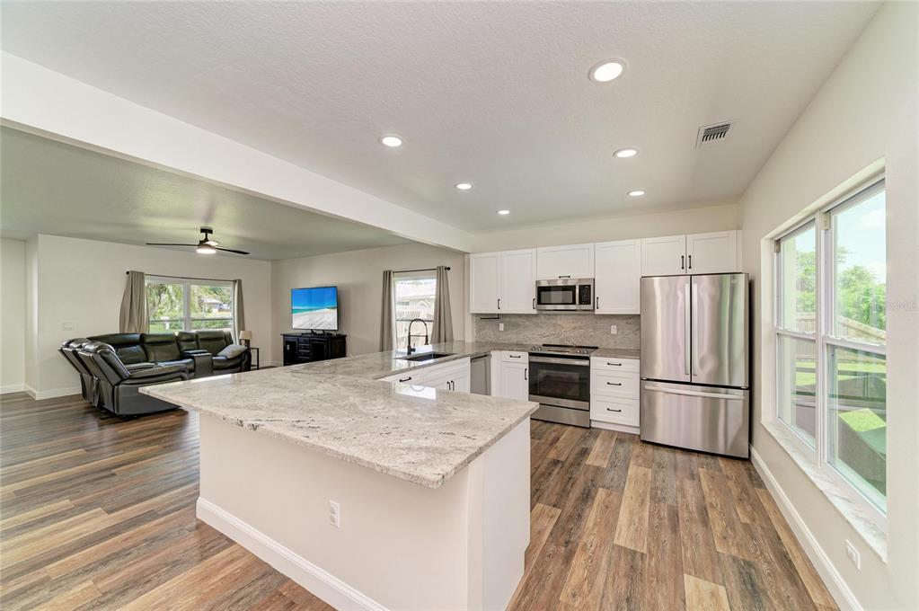 An open-concept kitchen features white cabinets, granite countertops, stainless steel appliances, and wood-look flooring — 3220 37TH TERRACE E, BRADENTON, FL