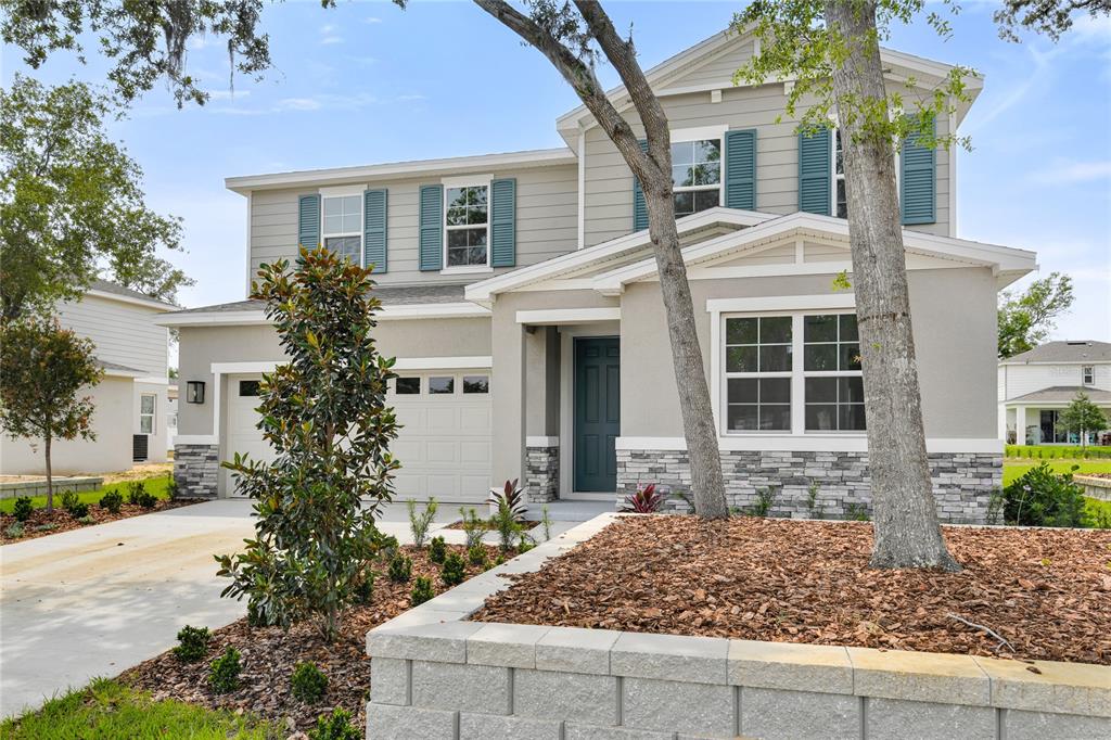 A two-story suburban house with a gray exterior, stone veneer, and a concrete driveway — 1051 CLOUD RIDGE COURT, MOUNT DORA, FL