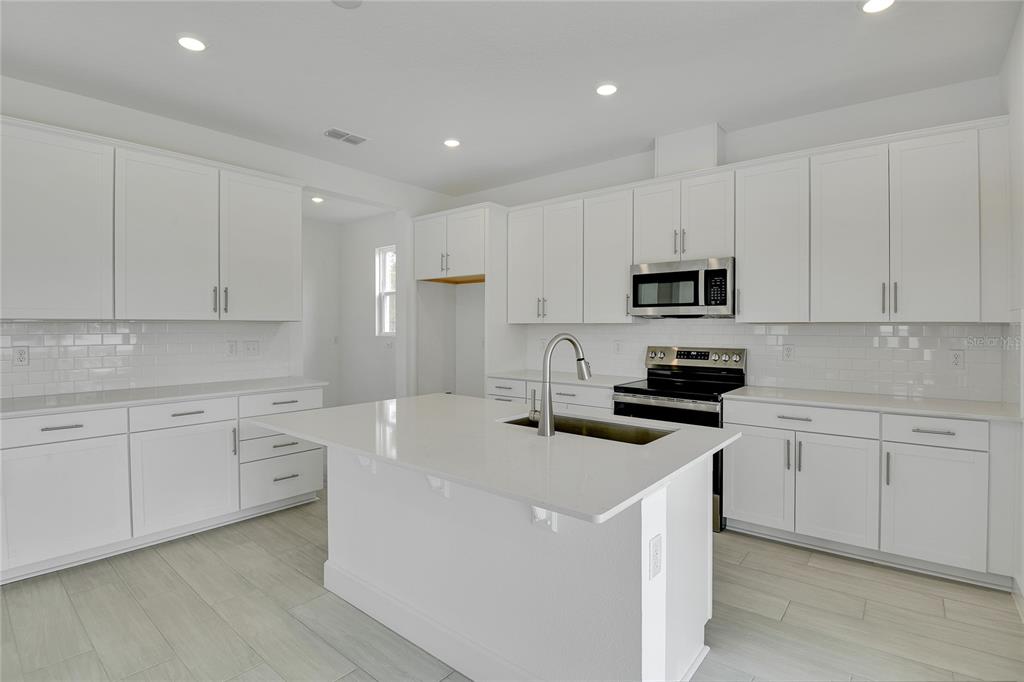 A modern white kitchen features a central island, quartz countertops, and stainless steel appliances — 1051 CLOUD RIDGE COURT, MOUNT DORA, FL