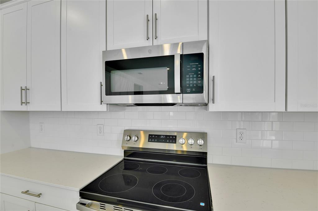 A kitchen features white cabinets, a stainless steel microwave, and a black electric range — 1051 CLOUD RIDGE COURT, MOUNT DORA, FL