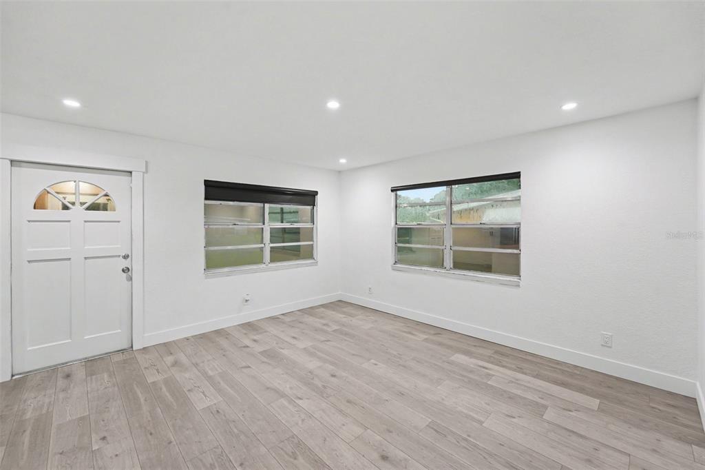An empty room with white walls, light wood-look flooring, two windows, and a front door — 131 EMERALD LANE, LARGO, FL