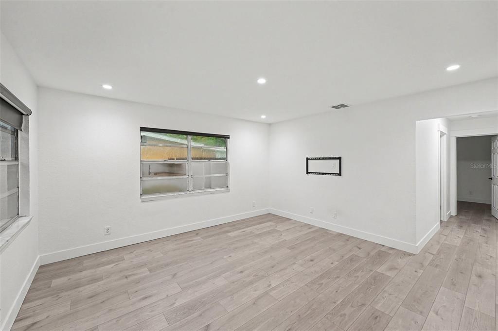 A bright, empty room features white walls, light wood-look flooring, and a window — 131 EMERALD LANE, LARGO, FL
