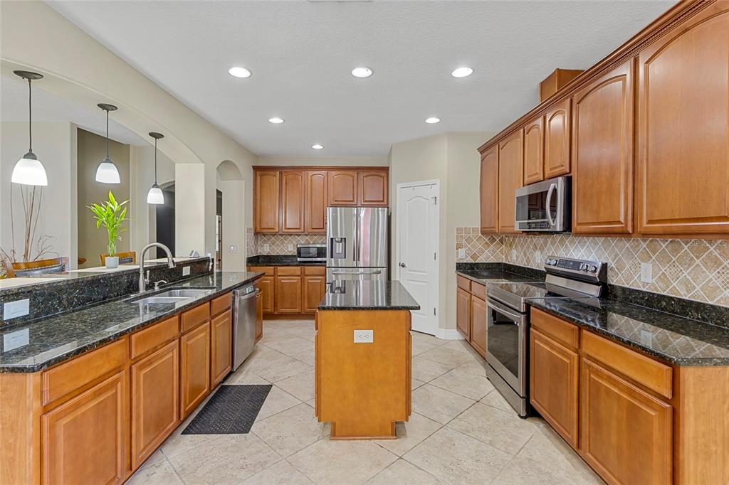 A kitchen features wood cabinets, dark granite countertops, stainless steel appliances, and a center island — 1945 ABBEY RIDGE DRIVE, DOVER, FL