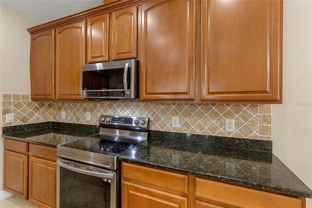 A kitchen features wood cabinets, dark granite countertops, a stainless steel stove, and tiled backsplash — 1945 ABBEY RIDGE DRIVE, DOVER, FL
