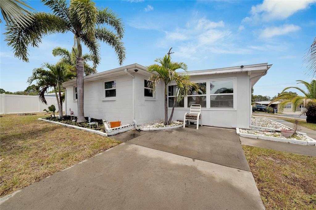 A white single-story house exterior features a concrete driveway, palm trees, and a small patio — 12093 104TH LANE, LARGO, FL