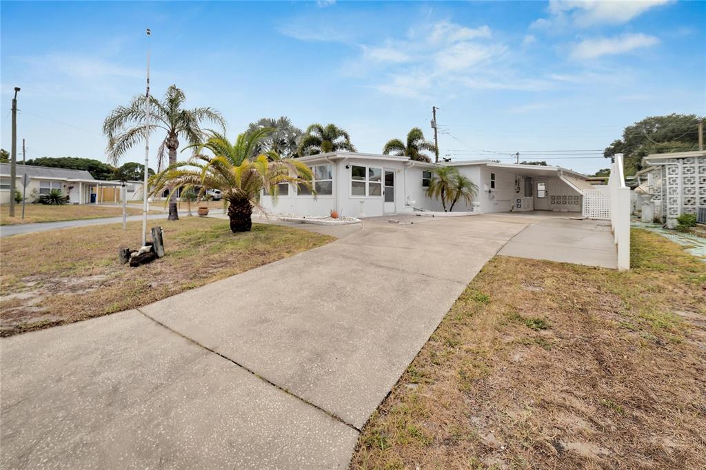 A single-story white house with a concrete driveway, carport, and palm trees in the yard — 12093 104TH LANE, LARGO, FL