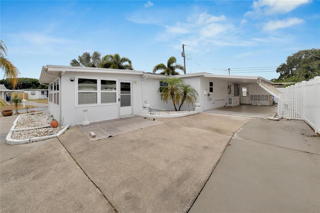 A white single-story house with a concrete driveway, carport, and small landscaped rock garden — 12093 104TH LANE, LARGO, FL