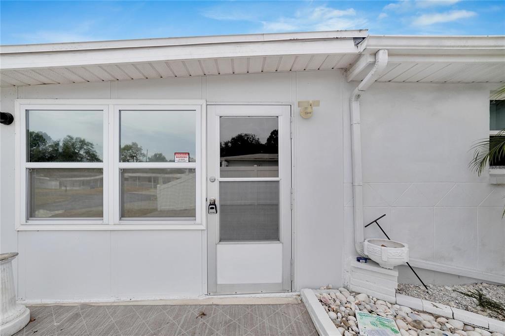 A white exterior wall features a screen door, adjacent windows, and a downspout — 12093 104TH LANE, LARGO, FL