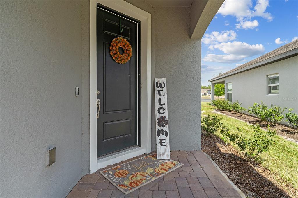 A dark front door with a wreath and a welcome sign sits on a porch — 3415 FEATHERGRASS CT, ST CLOUD, FL