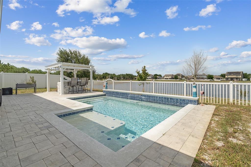 A backyard features a small swimming pool, a pergola with a bar, and white fencing — 3415 FEATHERGRASS CT, ST CLOUD, FL