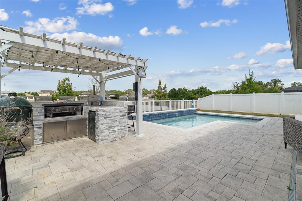A backyard patio features a stone outdoor kitchen, a pergola, and a swimming pool — 3415 FEATHERGRASS CT, ST CLOUD, FL