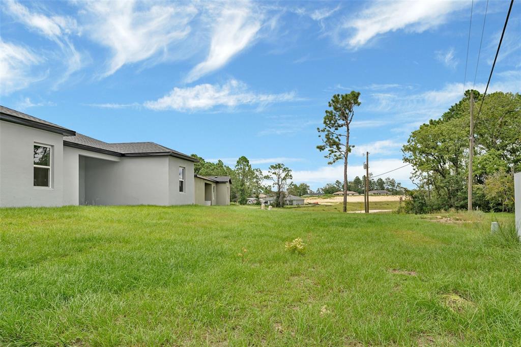 A grassy backyard area sits beside a modern gray house under a blue sky — 15301 SW 50TH AVENUE ROAD, OCALA, FL